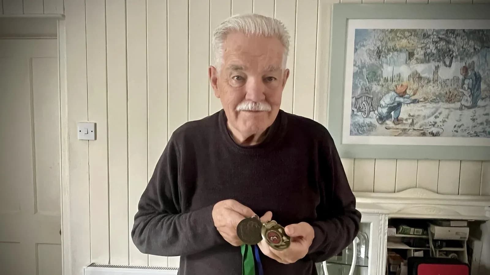Elderly man holding medals in living room