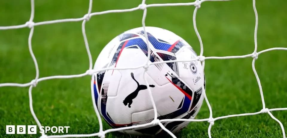Football resting in goal net on grass pitch