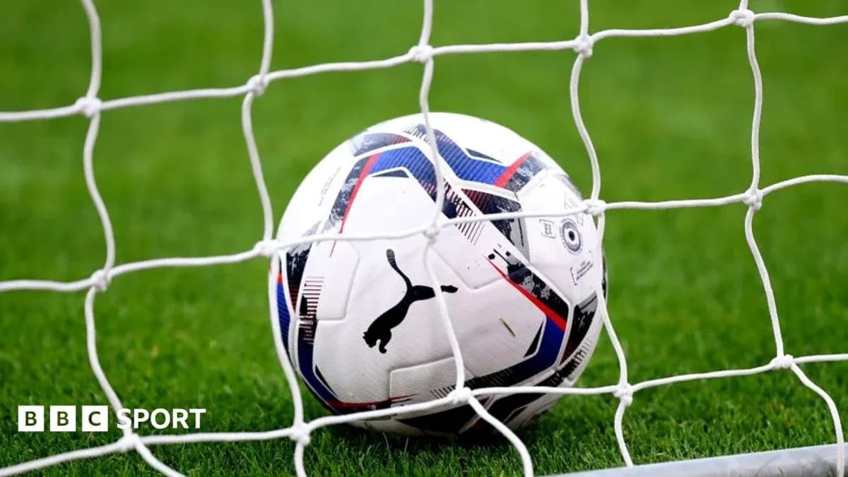 Football resting in goal net on grass pitch