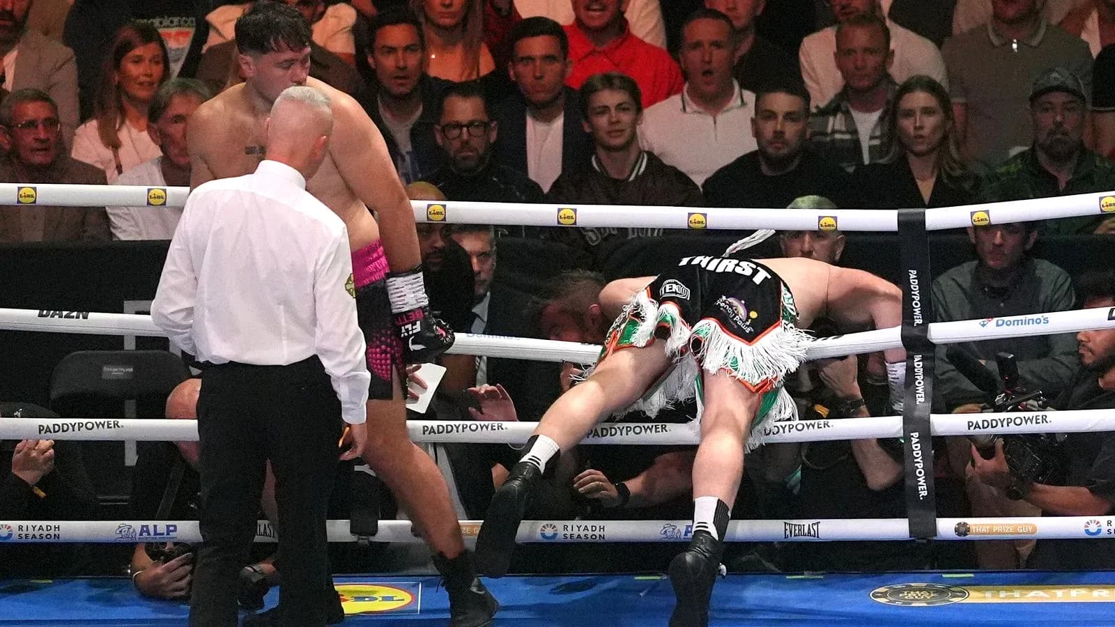 Boxer falling through ropes with referee observing