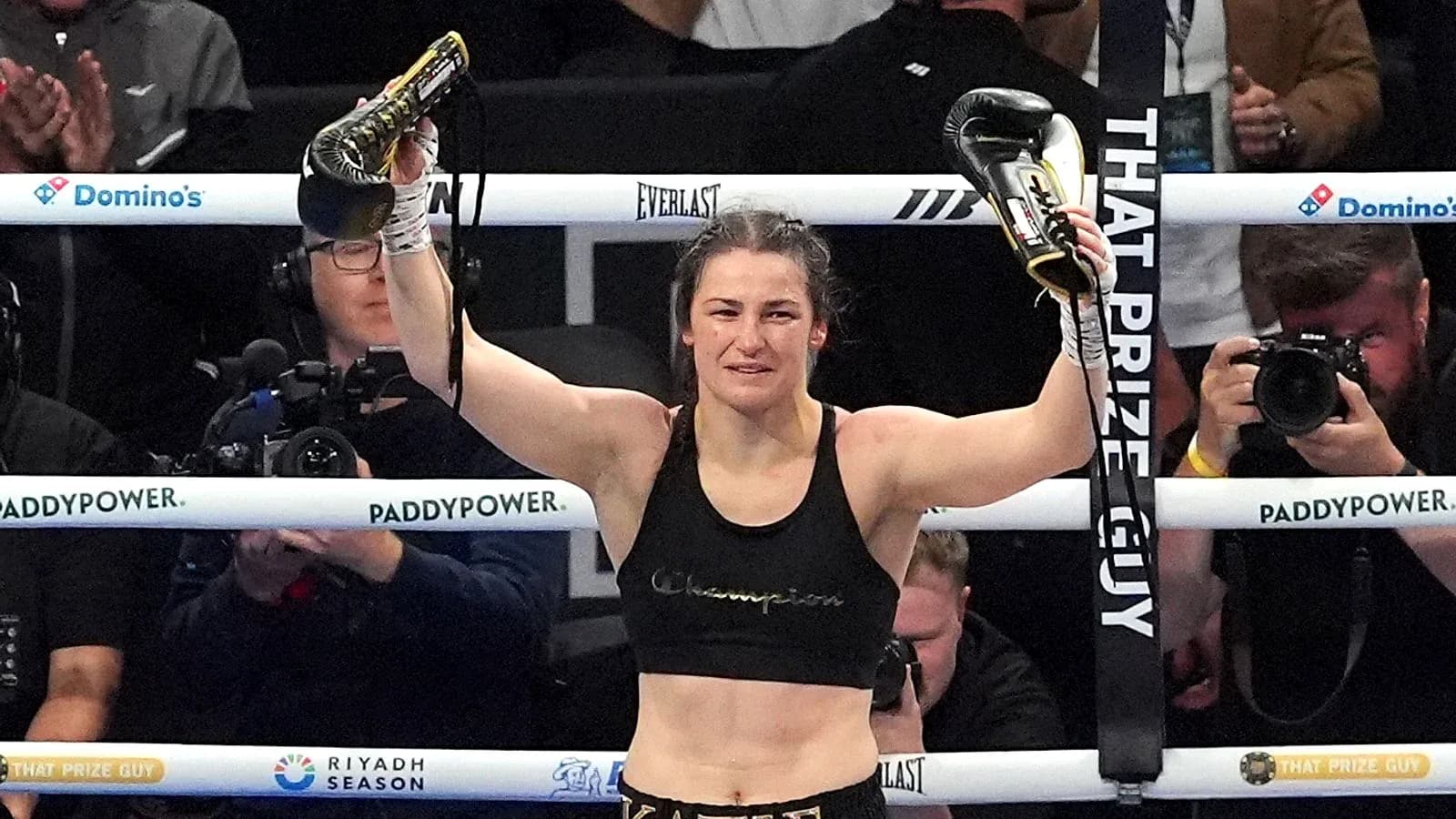 Female boxer celebrating with championship belts in ring