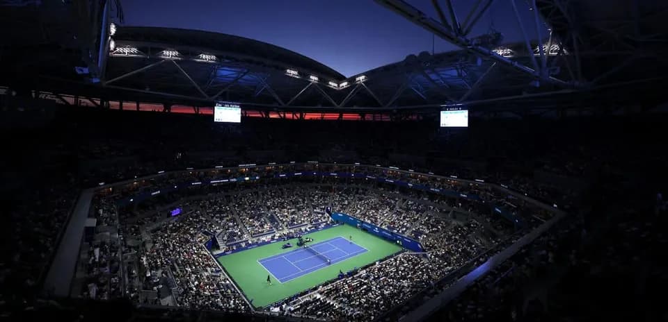 Crowd watching tennis match at night in stadium