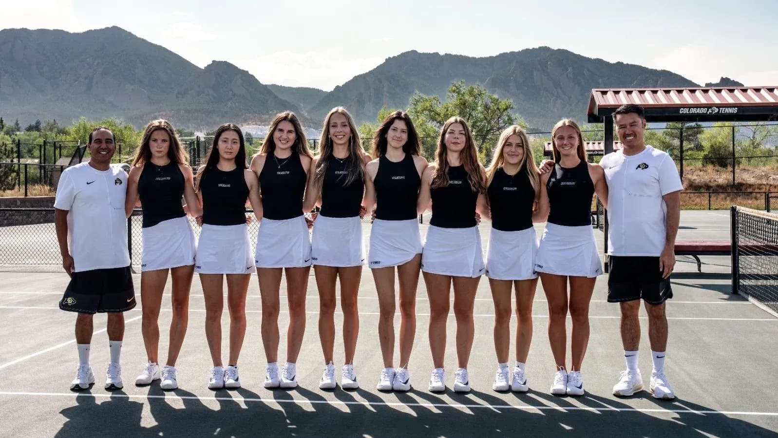 Tennis team posing together on court with coaches