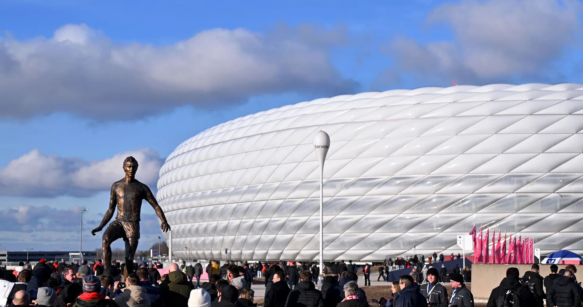 Crowd gathered near stadium with statue in foreground