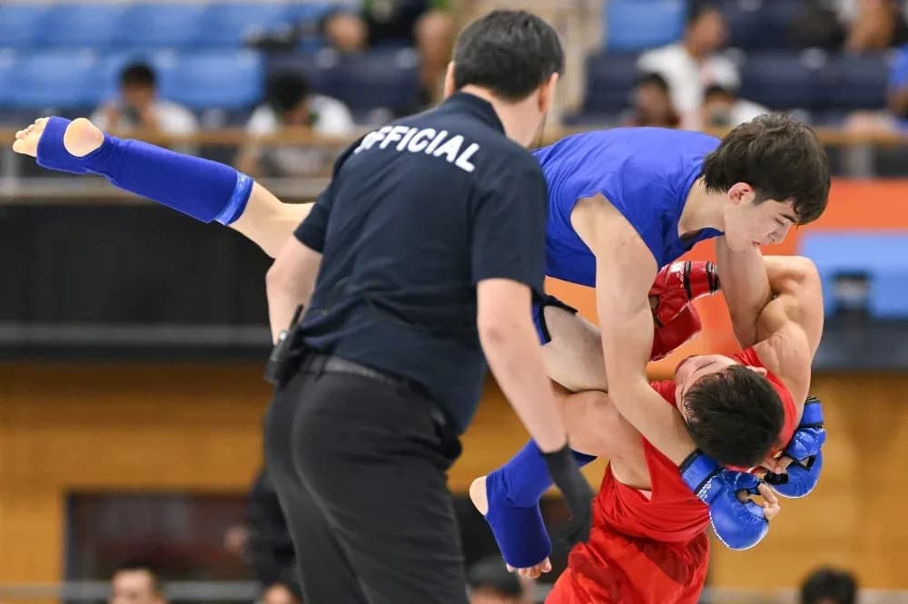 Athletes competing in grappling match with referee present