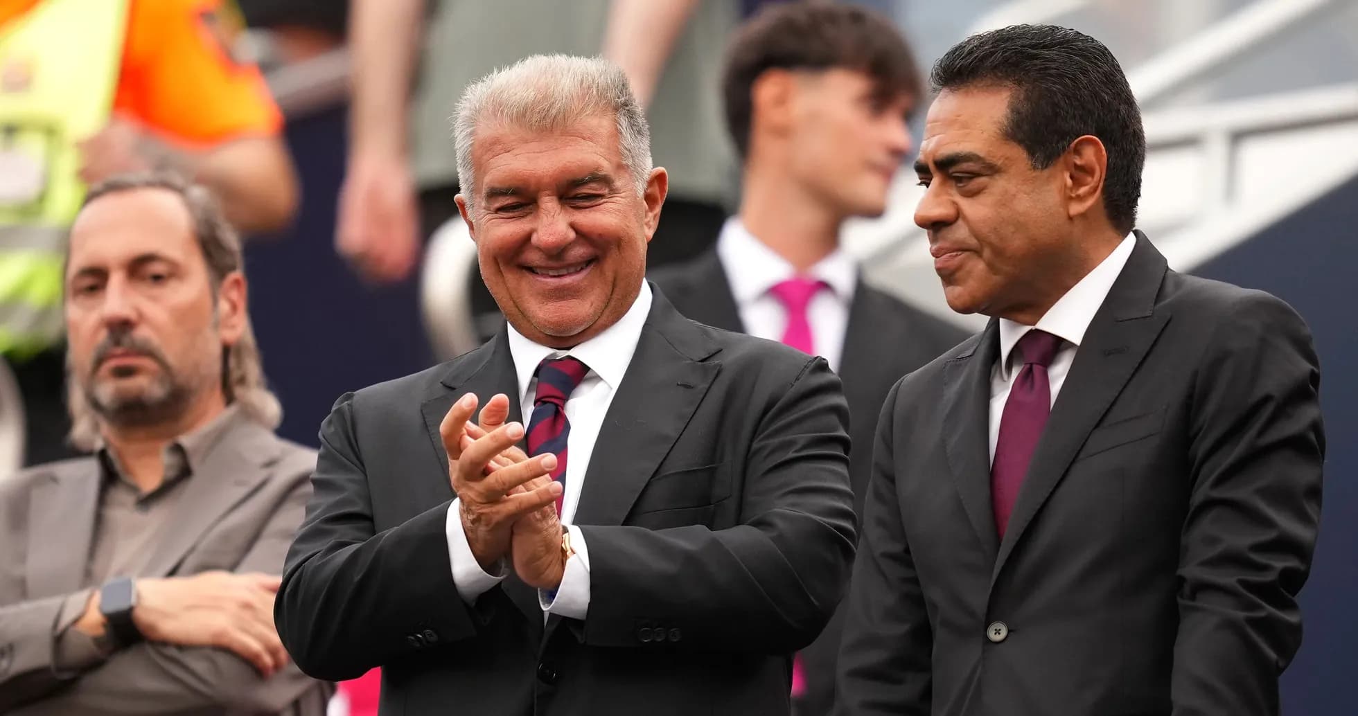 Three men in suits, one clapping, during event