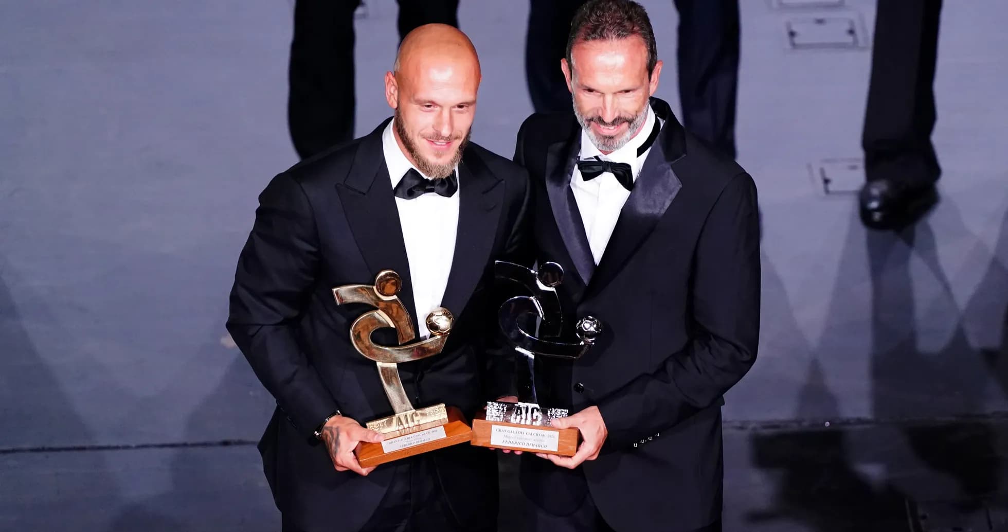 Two men in tuxedos holding awards at event