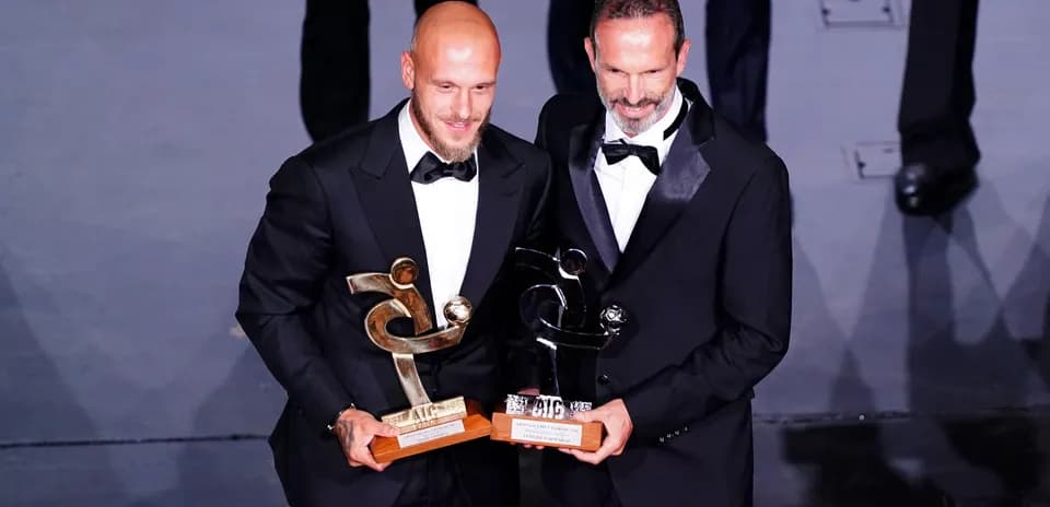 Two men in tuxedos holding awards at event