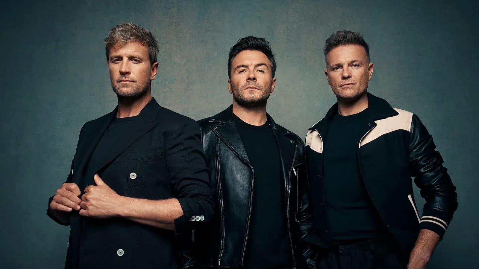 Three men posing in stylish outfits against a backdrop