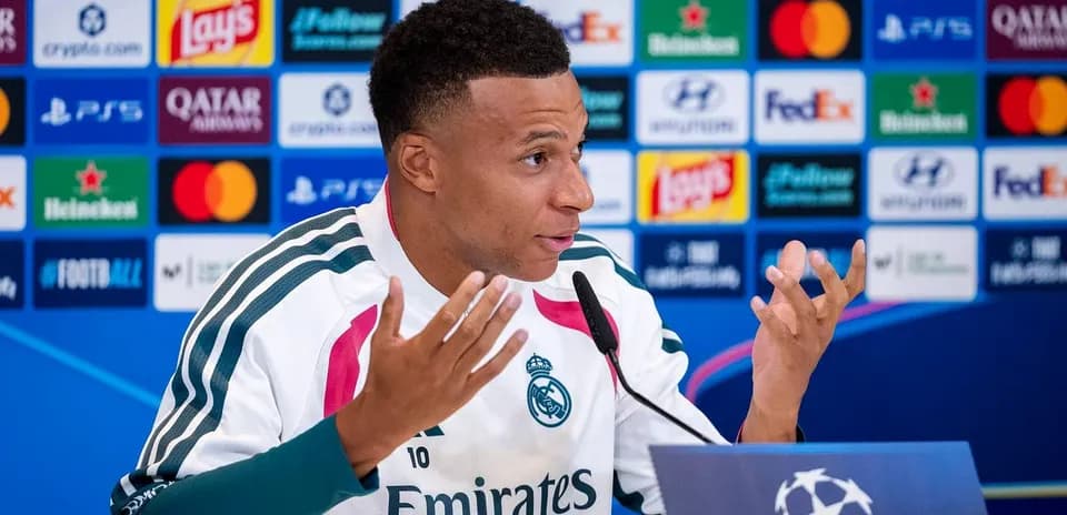 Player speaking at press conference with logos in background