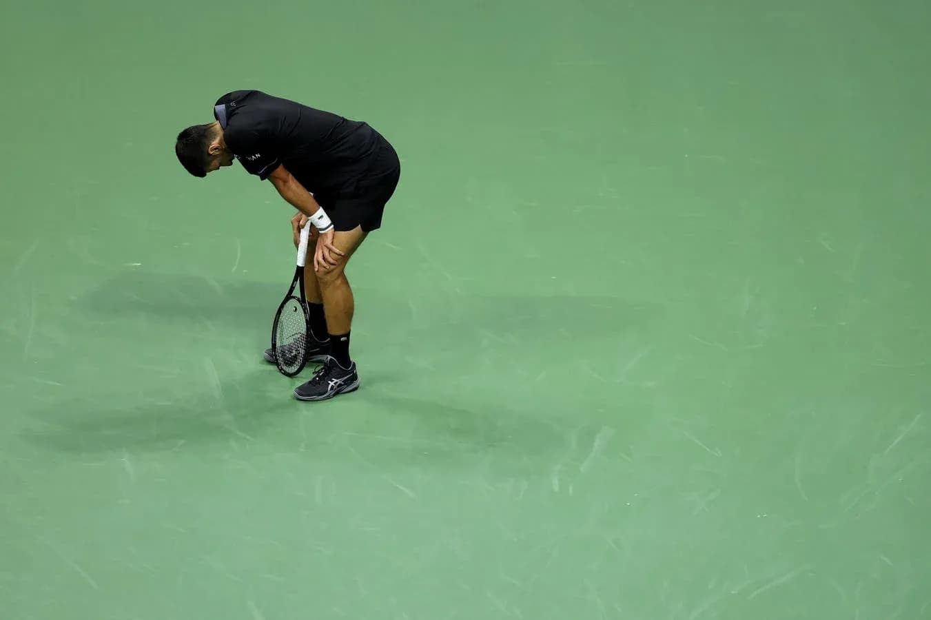 Tennis player bending over with racket on court