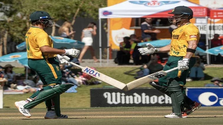 Two cricket players celebrating with their bats