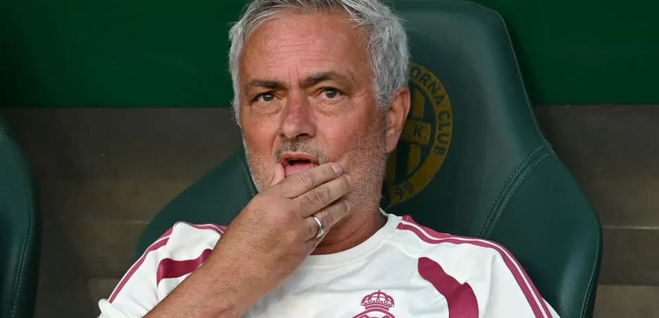 Coach sitting on bench during match, hand on face