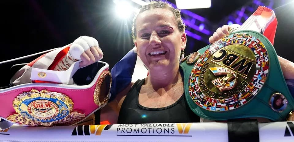 Female boxer celebrating with championship belts in ring