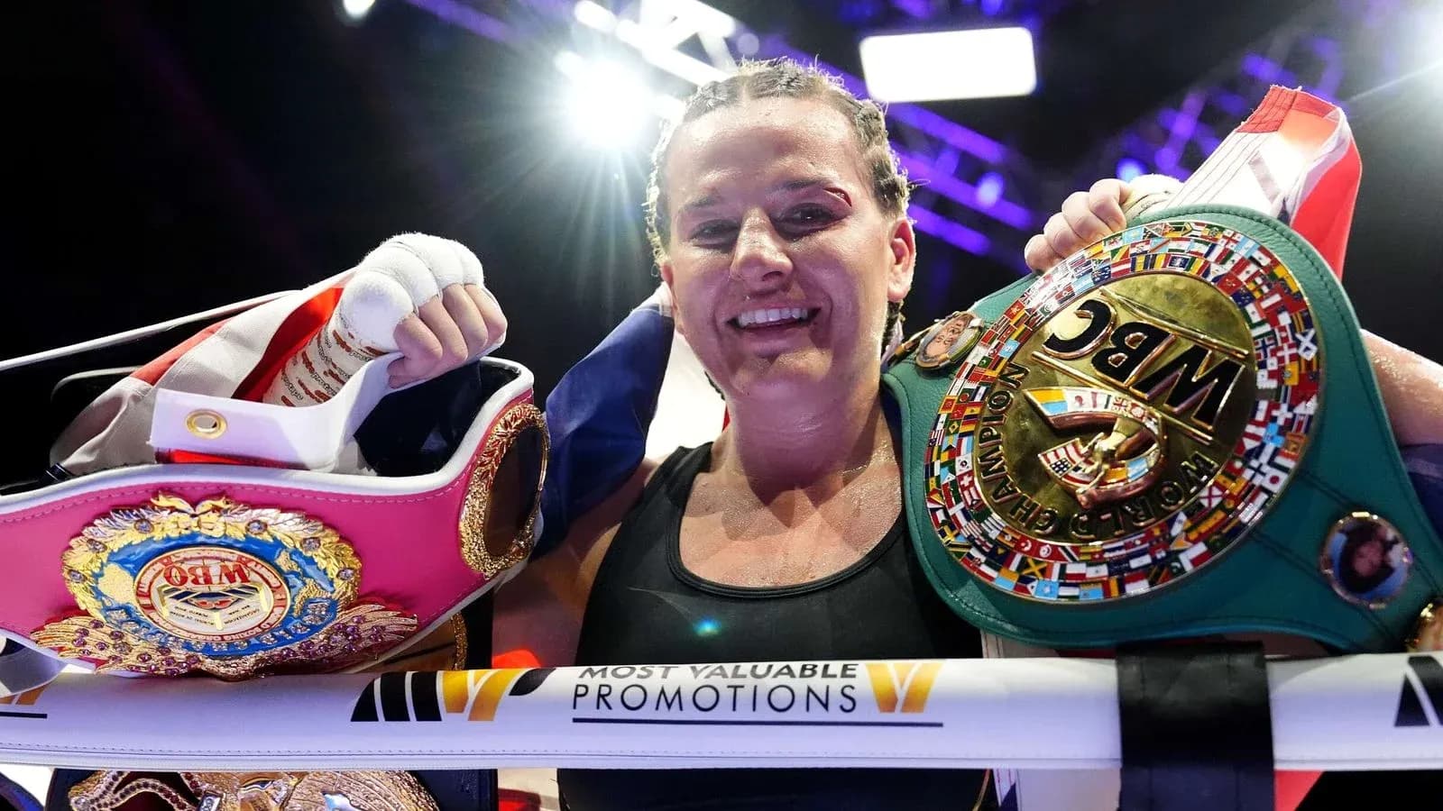 Female boxer celebrating with championship belts in ring