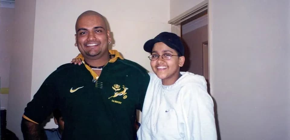 Two individuals posing together indoors, smiling
