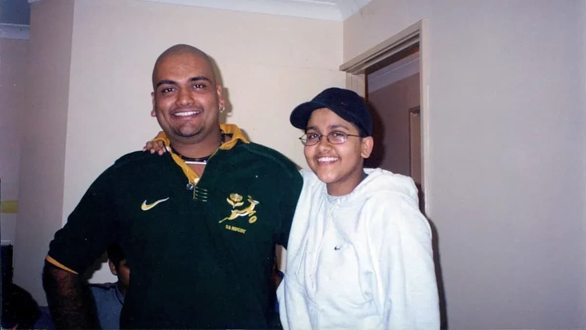 Two individuals posing together indoors, smiling