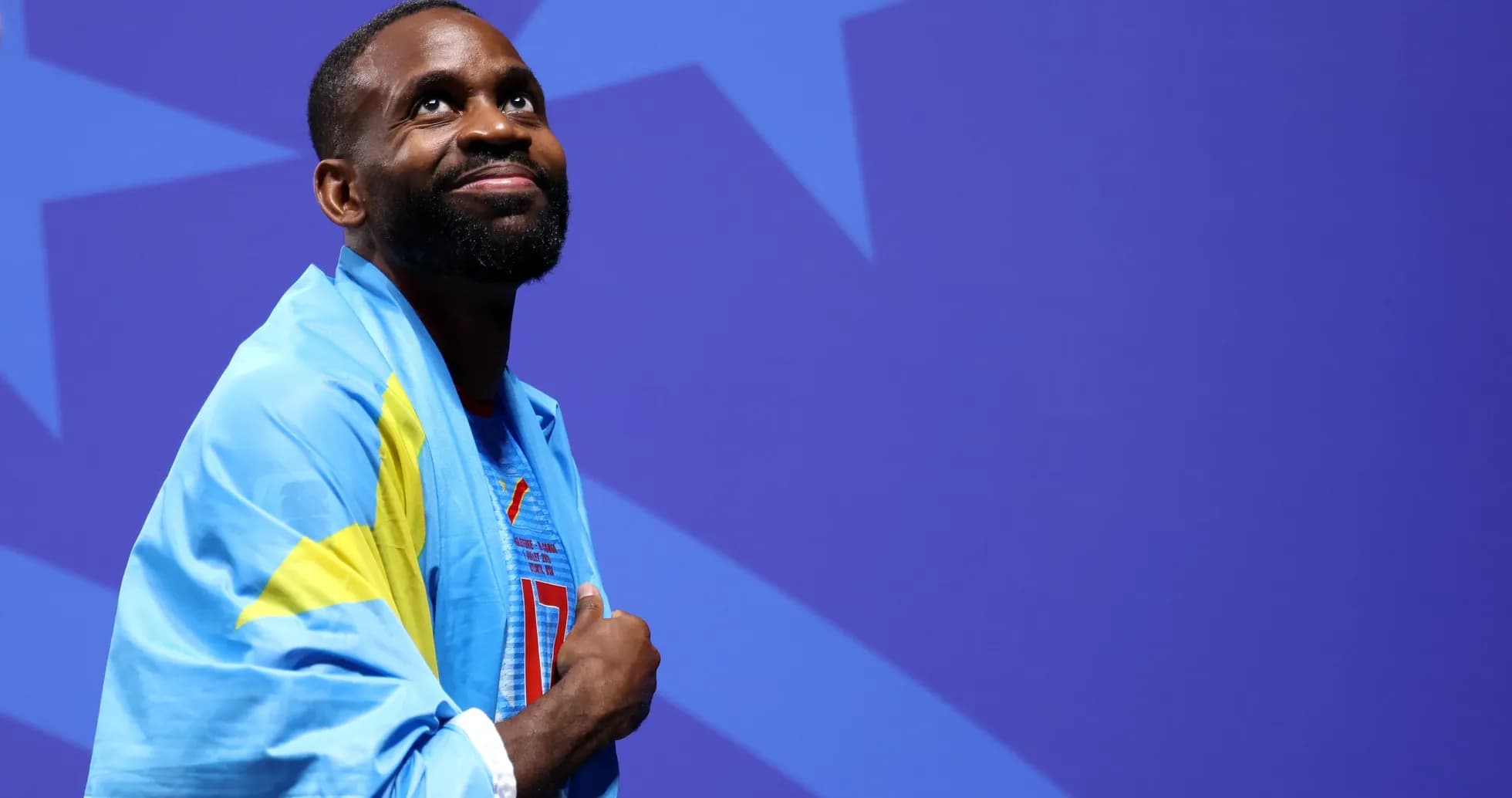 Athlete wrapped in flag, looking upward on stage Athlete wrapped in flag, looking upward on stage